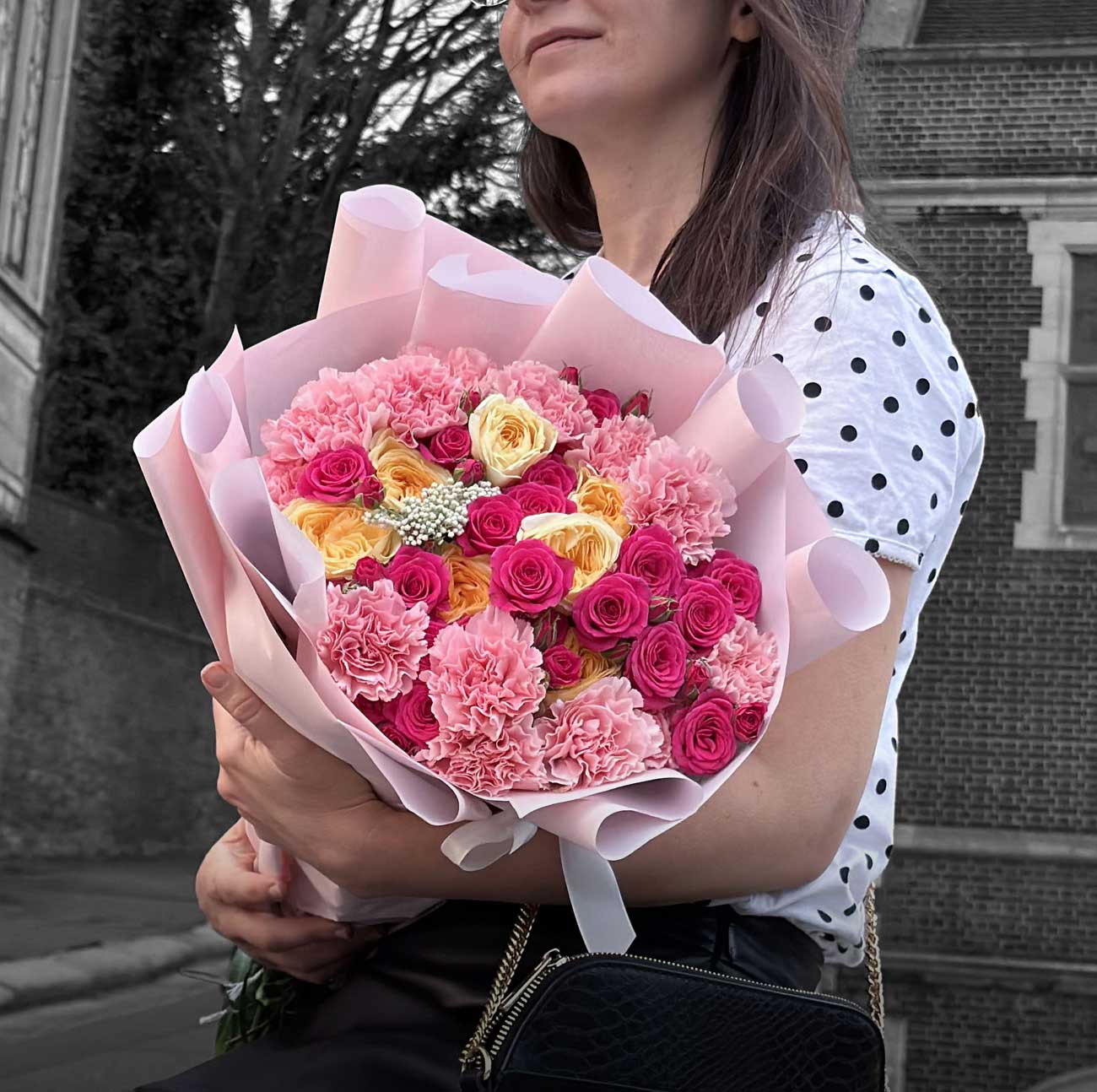 Person holding a bouquet of pink and yellow flowers outdoors.