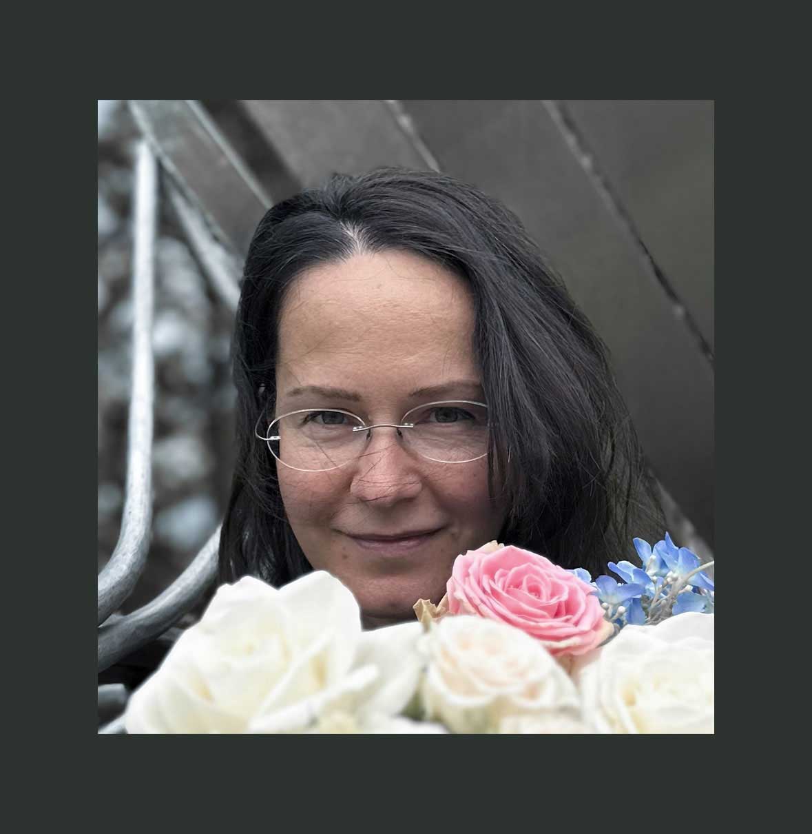 Woman with glasses holding a bouquet of flowers against a blurred background
