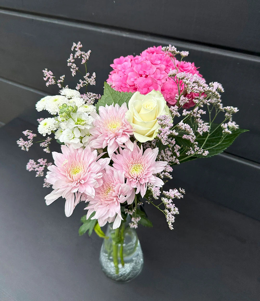 Bouquet of pink, white, and green flowers in a clear vase on a dark surface.