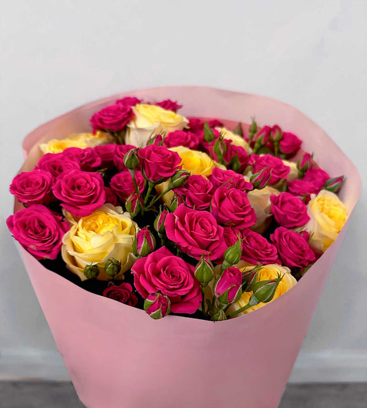 Bouquet of pink and yellow roses in a pink wrap against a light gray background